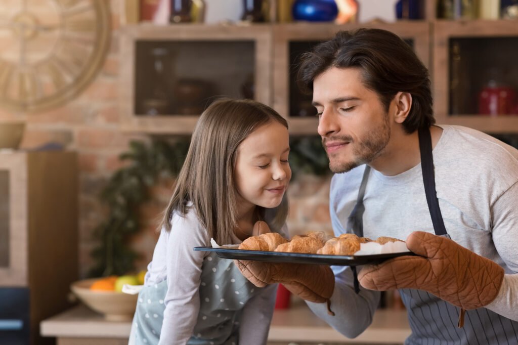 Homemade pastries. Cute little girl and dad smelling freshly baked croissants with her father